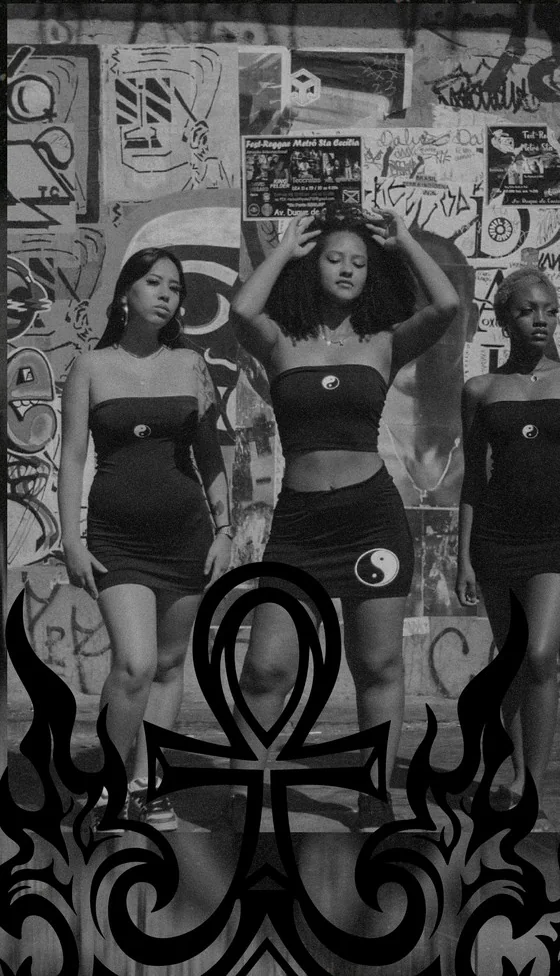 Três mulheres em preto e branco diante de uma parede de grafite, com a ankh e as chamas da marca em primeiro plano